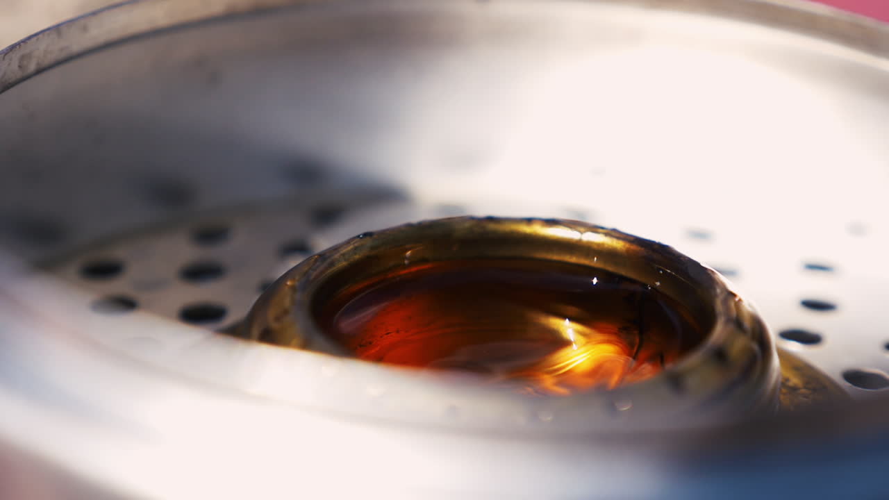 화창한 날 호수에서 요리하기 위해 trangia 휴대용 스토브에 타는 액체를 붓습니다.