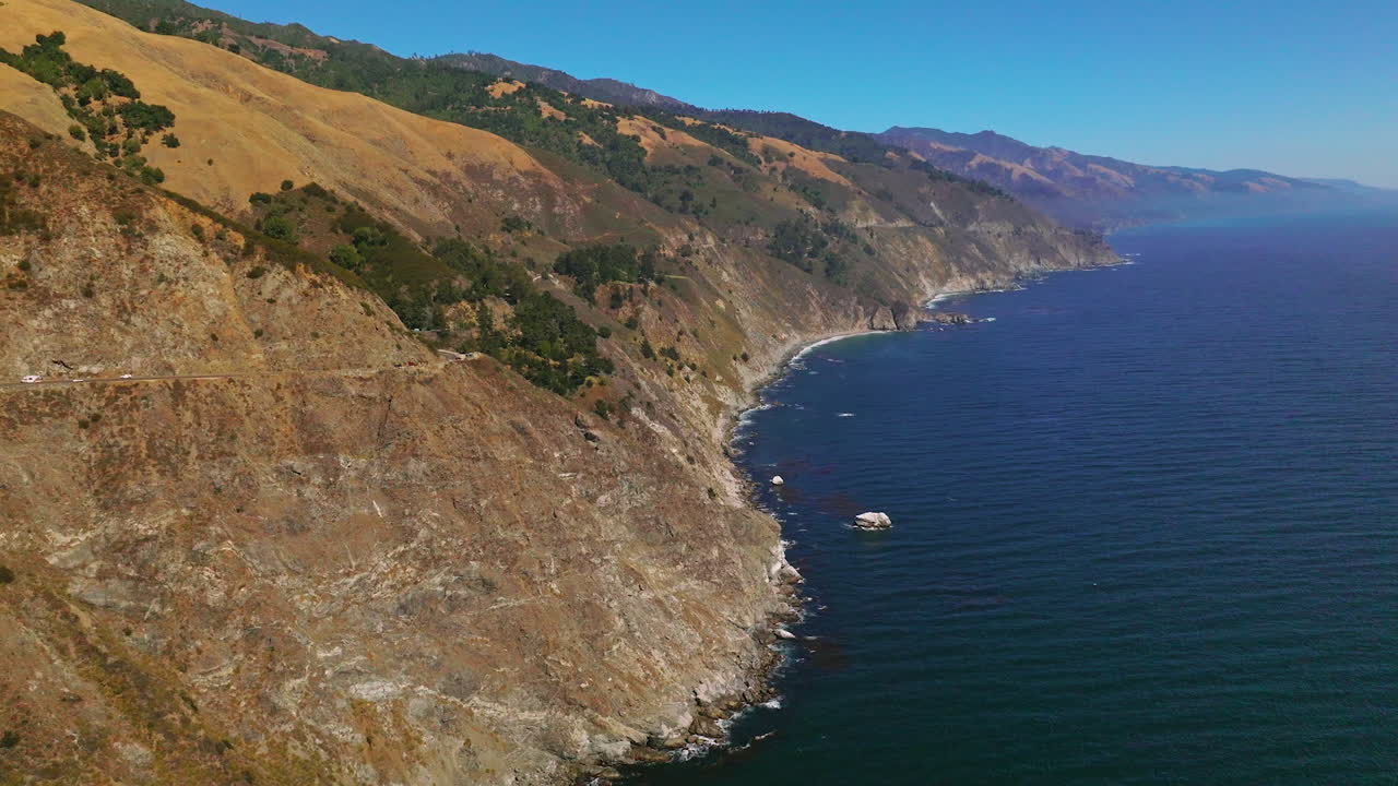 Flying over the mountains descending into the deep ocean. Wonderful scenery of amazing rocky landscape on sunny day in Big Sur Morro Bay, California, United States.