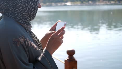 woman in hijab taking photo by the lake