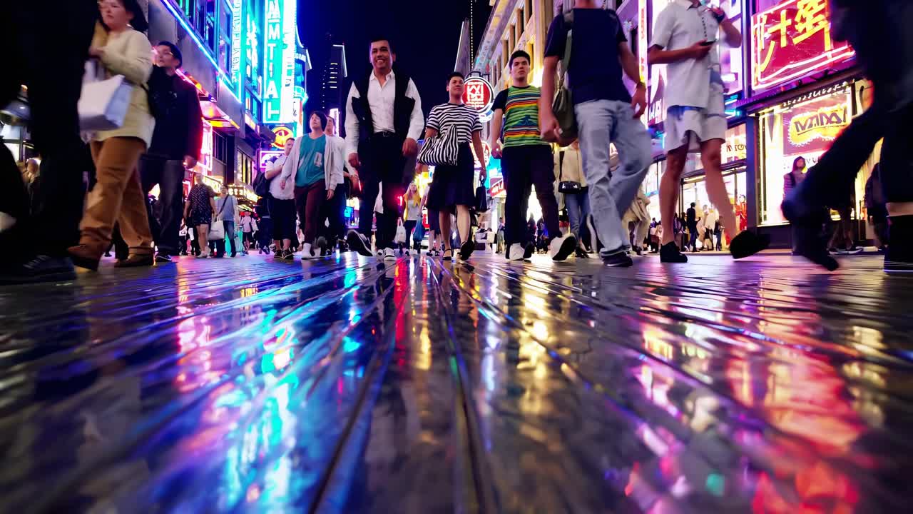 Low-angle video shot of people's feet walking on a wet, reflective street, surrounded by vibrant