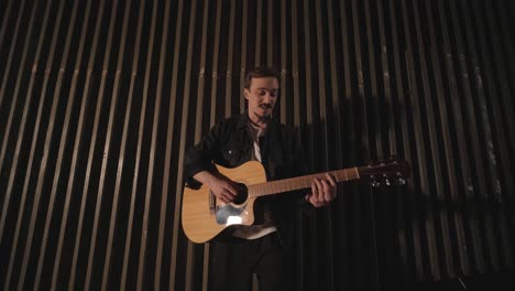 a handsome guy plays an acoustic guitar in an abandoned cinema. the musician sings a song and accompanies on the guitar