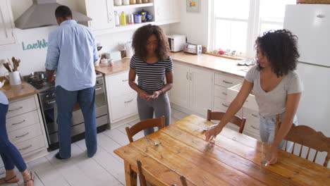 family with teenage children laying table for meal in kitchen