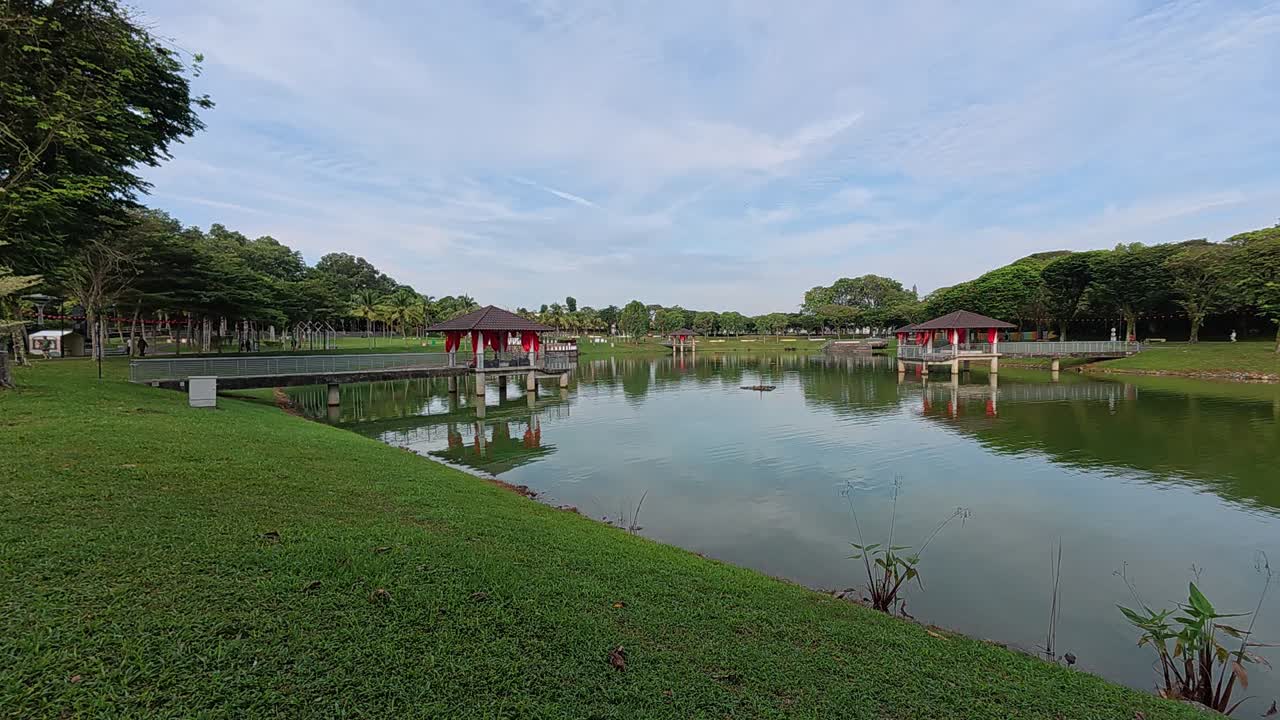 A tranquil lake in a tropical public park surrounded by lush greenery. Visitors enjoy recreation and relaxation in this serene setting.