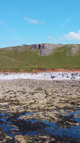 vertical video pushing drone shot on rocky beach with coastal erosion and winding coast path with multiple rock pools and seaweed.