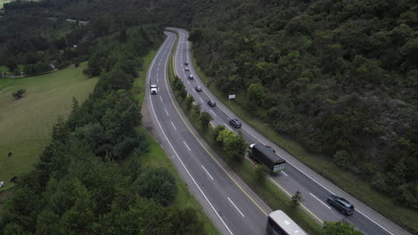 aerial shot captures the beauty of cars driving along a winding countryside road, as they disappear into the sunset. the stunning landscape features rolling hills, fields, and farmland.