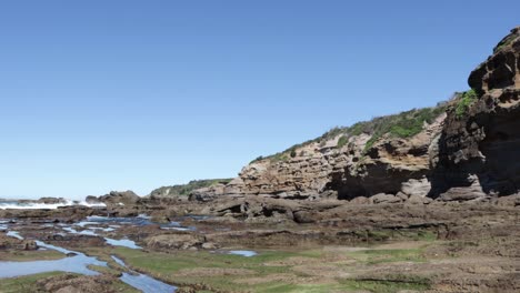 Rock-cliffs-at-Cave-beach-on-Jervis-Bay-Australia-with-tidepool-area-washed-by-ocean-waves,-Locked-shot