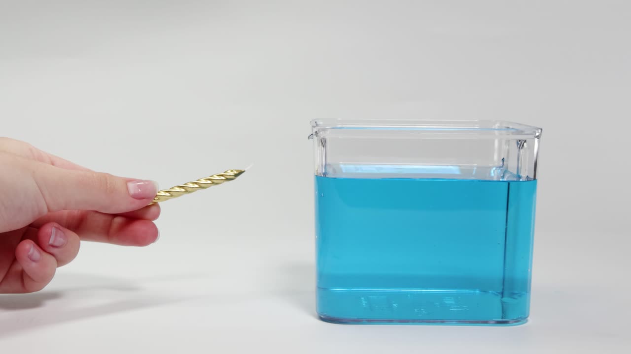 A hand places a gold object into blue liquid, observing its buoyancy and movement