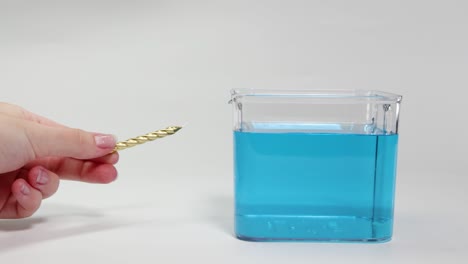 a hand places a gold object into blue liquid, observing its buoyancy and movement