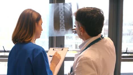 Doctor-examining-x-ray-while-nurse-writing-on-clipboard