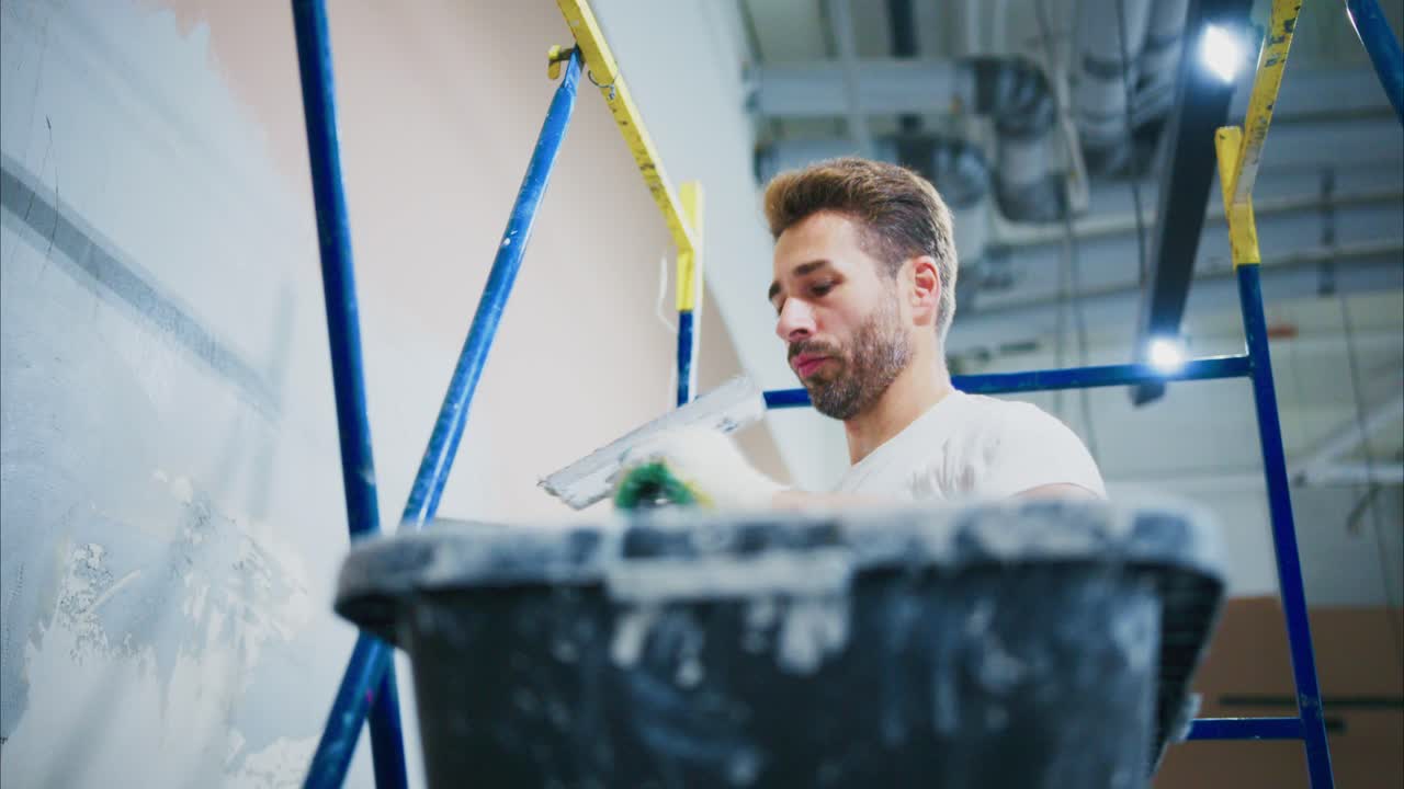 A Focused Worker Skillfully Applies Drywall Compound on a Wall While Balancing on a Ladder, Demonstrating Precision and Attention to Detail in a Renovation Project