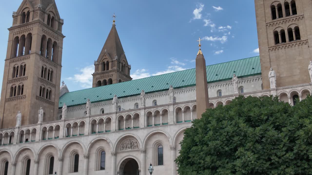 Pan from the tower spires of Pécs Cathedral down to the main facade, highlighting ornate details and baroque architectural elegance