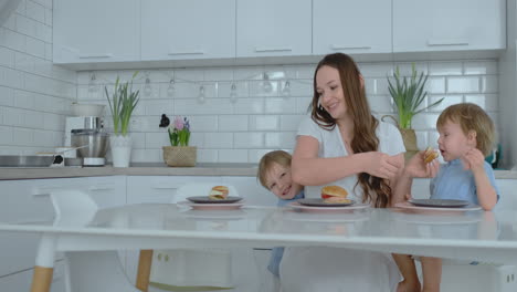 mom helps her little son eat a burger in the kitchen