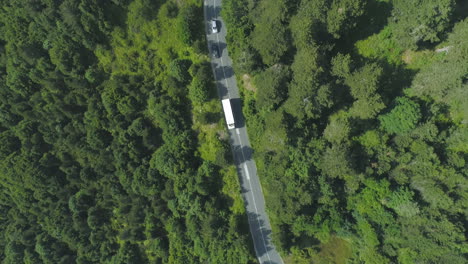 Top-view-of-White-bus-followed-by-two-cars-driving-on-curvy-forest,-asphalt-road