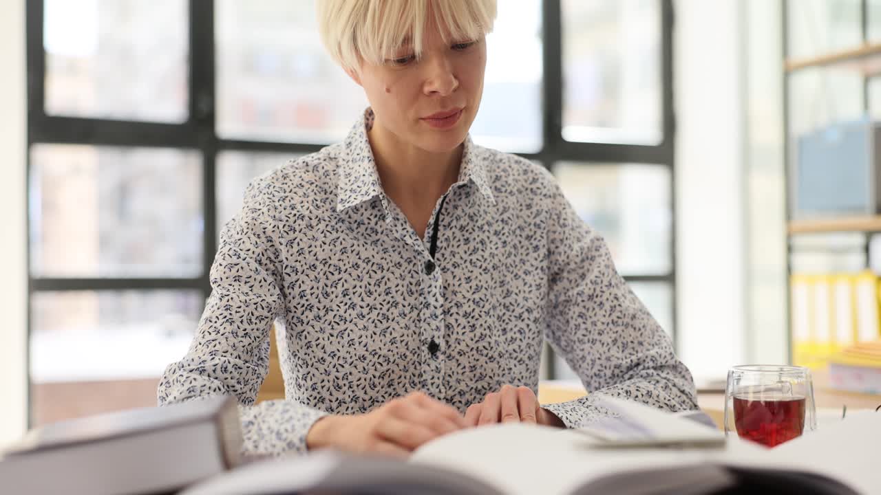 Fokuseret kvindelig studerende læser bøger for at finde information til sin opgave