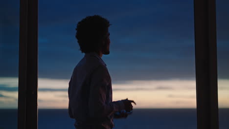 young man using smartphone in hotel room texting sharing vacation lifestyle on social media enjoying view of ocean at sunset