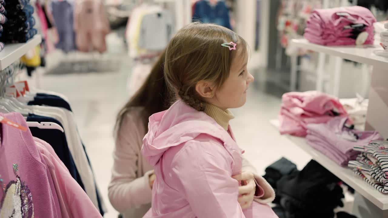Mother with daughter in shopping mall trying pink jacket
