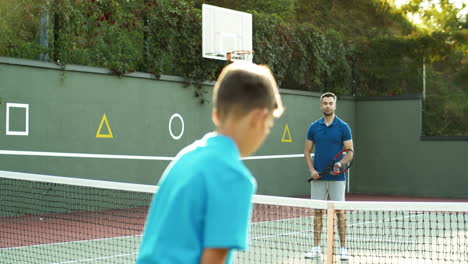 rear view of a teen boy playing tennis with his dad on a sunny day