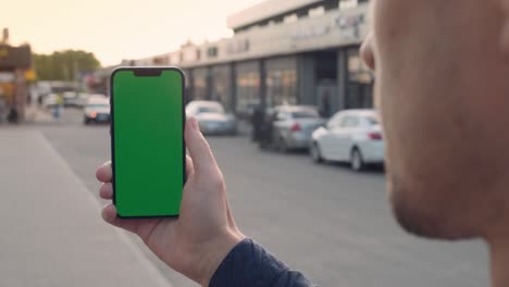 la mano de un hombre de primer plano sosteniendo un teléfono inteligente pantalla de maqueta verde llave de croma al aire libre