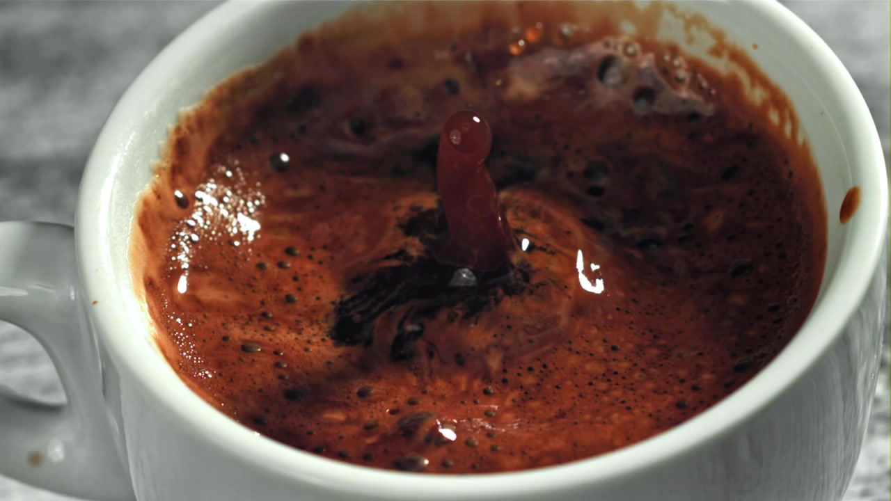 Primo piano di una goccia che schizza nel caffè caldo al rallentatore.