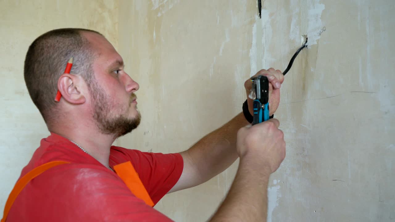 Electrician with pliers cleaning wires in junction box for socket