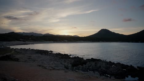 Zeitraffer-Des-Spanischen-Sonnenuntergangs-Mit-Den-Bergen-Mallorcas-Am-Strand-Mit-Klarem-Wasser