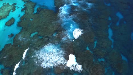 a drone captures a mesmerizing shot of a blue lagoon reef with waves crashing during the day, showcasing the reef's vast beauty and the dynamic element of the waves