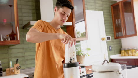 Hombre-Birracial-Enfocado-Preparando-Batido-De-Frutas-Con-Licuadora-En-La-Cocina,-Espacio-Para-Copiar,-Cámara-Lenta