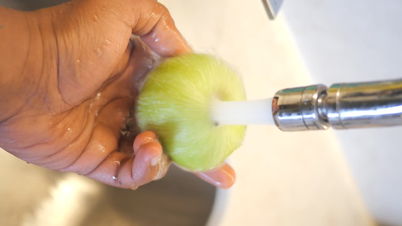 Persona lavando un chayote bajo el agua corriente en un fregadero