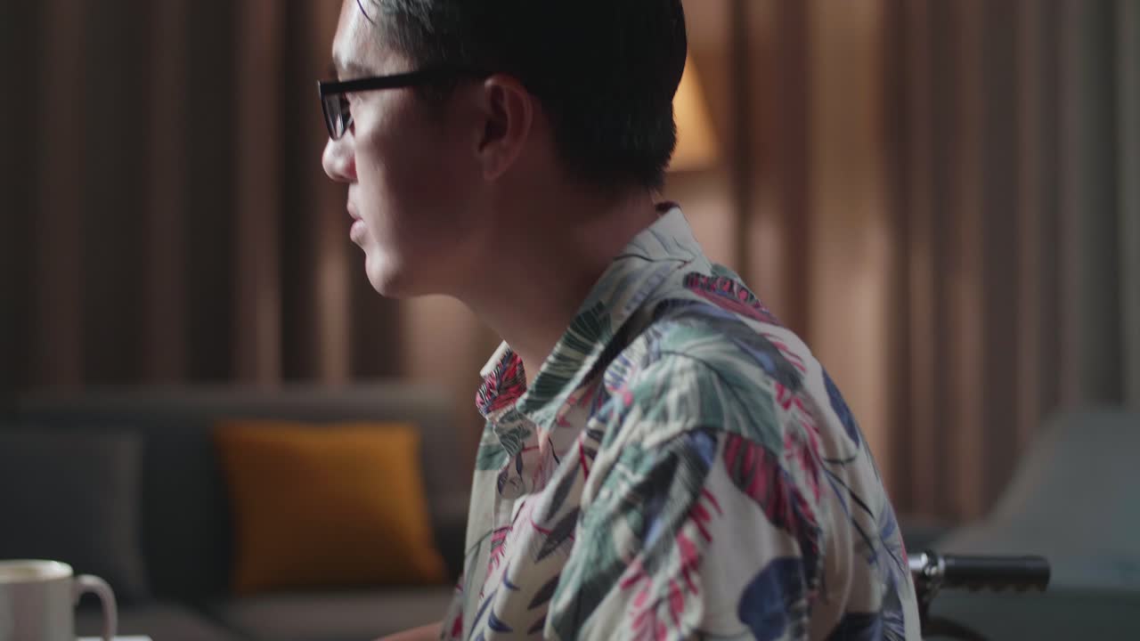 체어에 앉은 아시아인 남자가 집에서 데스크을 사용하여 비디오를 편집하고 있습니다.