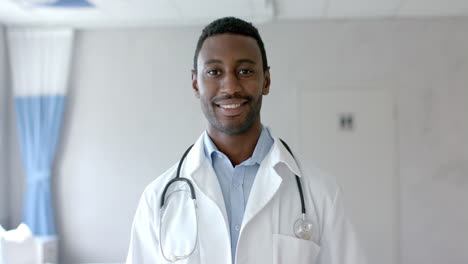 portrait of happy african american male doctor in white coat smiling in hospital ward, slow motion