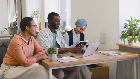 young worker working with laptop sitting at his desk while muslim businesswoman and businesswoman talk to him sitting at desk 2