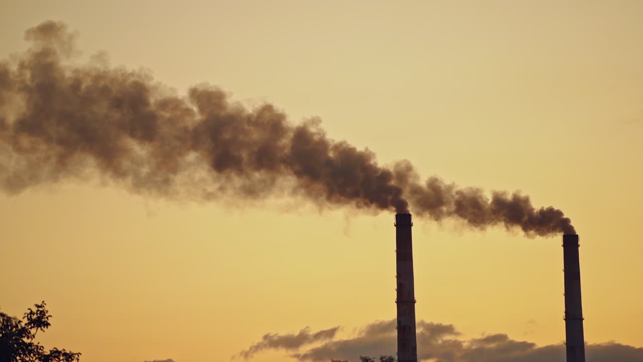 Dark smoke comes from large pipes into the air on the evening sky background. Dirty emissions pollute the environment. Ecological problems in the air.
