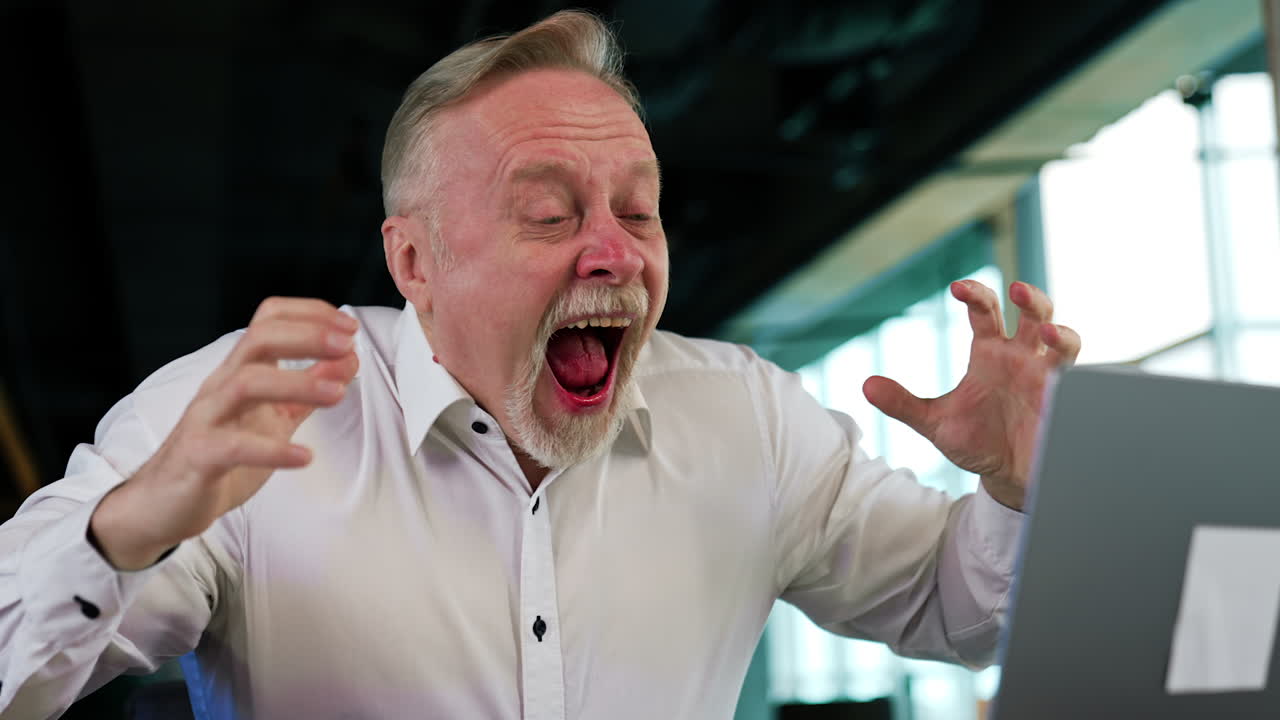 Astonished Caucasian mature businessman looking at his laptop. Man with a grimace of surprise changing into the expression of despair and disappointment. Close up.