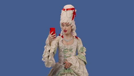 portrait of courtier lady in white vintage lace dress and wig talking for video chat using mobile phone. young woman posing in studio with blue screen background. close up. slow motion ready 59.94fps