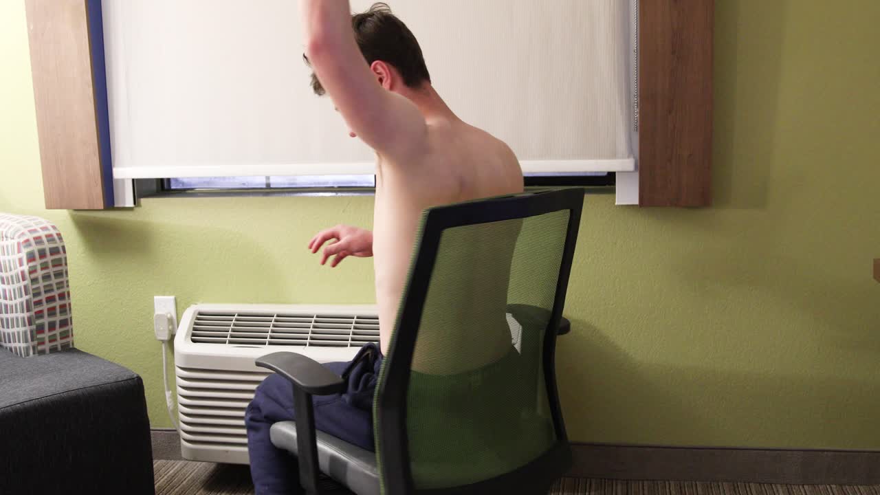 셔츠를 입지 않은 백인 백인 남성은 호텔 방 의자에서 돈을 떨어뜨리고 커튼이 그려진 밤에 은색으로 돈을 바꾼다