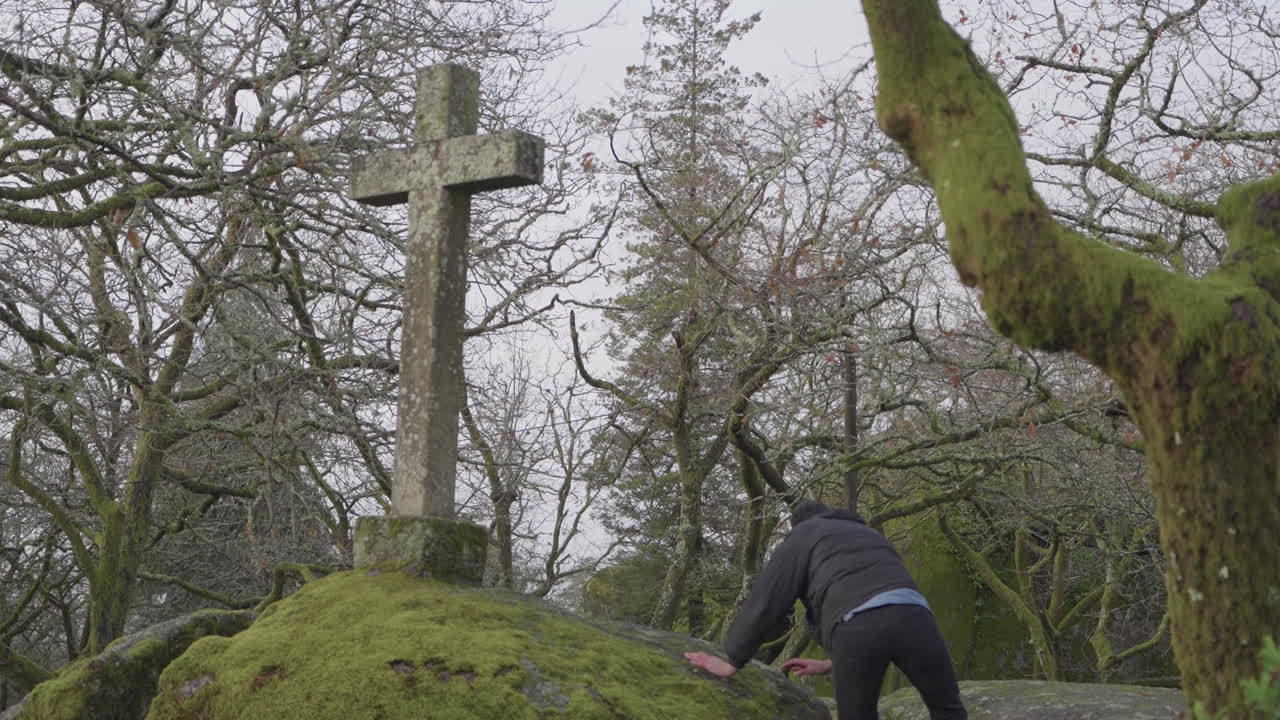 Uomo adulto che fa jogging accanto a una croce di pietra tra alberi spogli all'aperto.