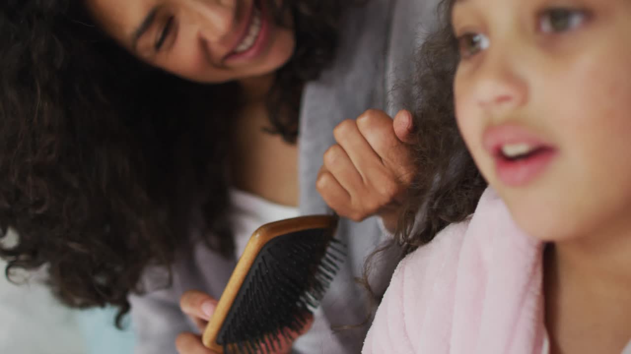 madre e hija de raza mixta feliz cepillando el cabello en el dormitorio
