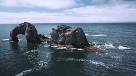 drone approach shot of a large and tall rock formation in the middle of the ocean with nothing else around it