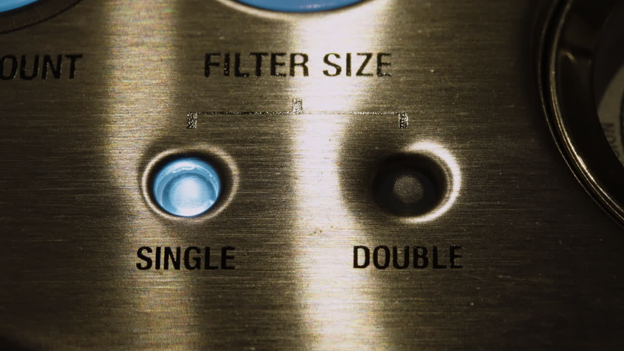 Ekstremt nærbillede af en professionel espressomaskines interface med blå LED-lys, der skifter mellem indstillinger for enkelt- og dobbeltfilterstørrelse