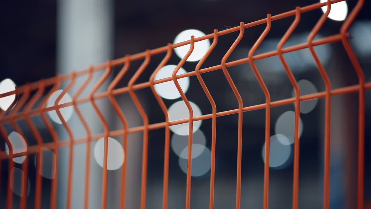 Modern orange fence made of metal mesh against the background of bright lights