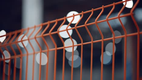 modern orange fence made of metal mesh against the background of bright lights