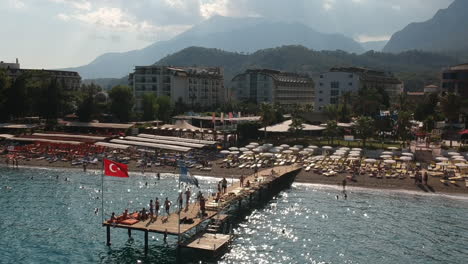 Aerial-drone-shot-of-people-swimming-and-sunbathing-on-a-pier-at-a-hotel-beach-in-Kemer,-Turkey
