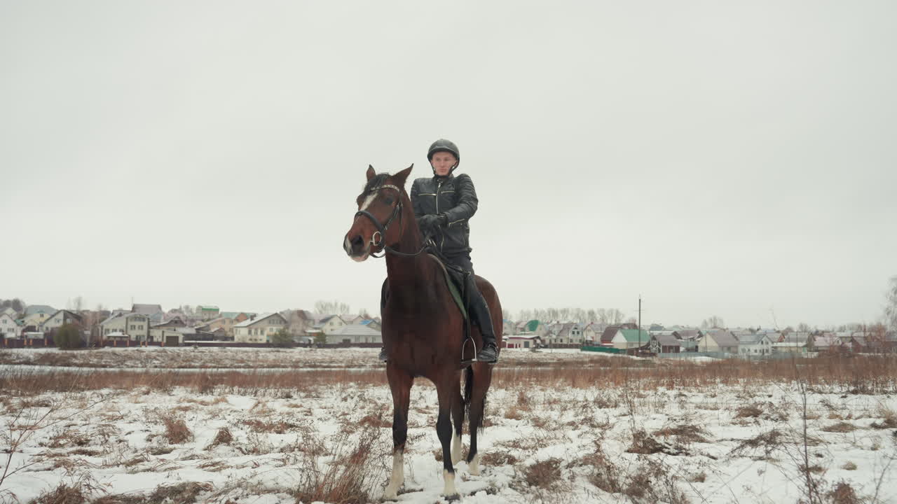 Una persona si avvicina a un cavallo su una pianura innevata, tentando esercizi di monta e coordinazione, uno studio del movimento del lavoro di squadra in tandem, con uno sfondo rurale e un cielo invernale tenue, ponendo l'accento sulla fiducia e sull'istruzione.