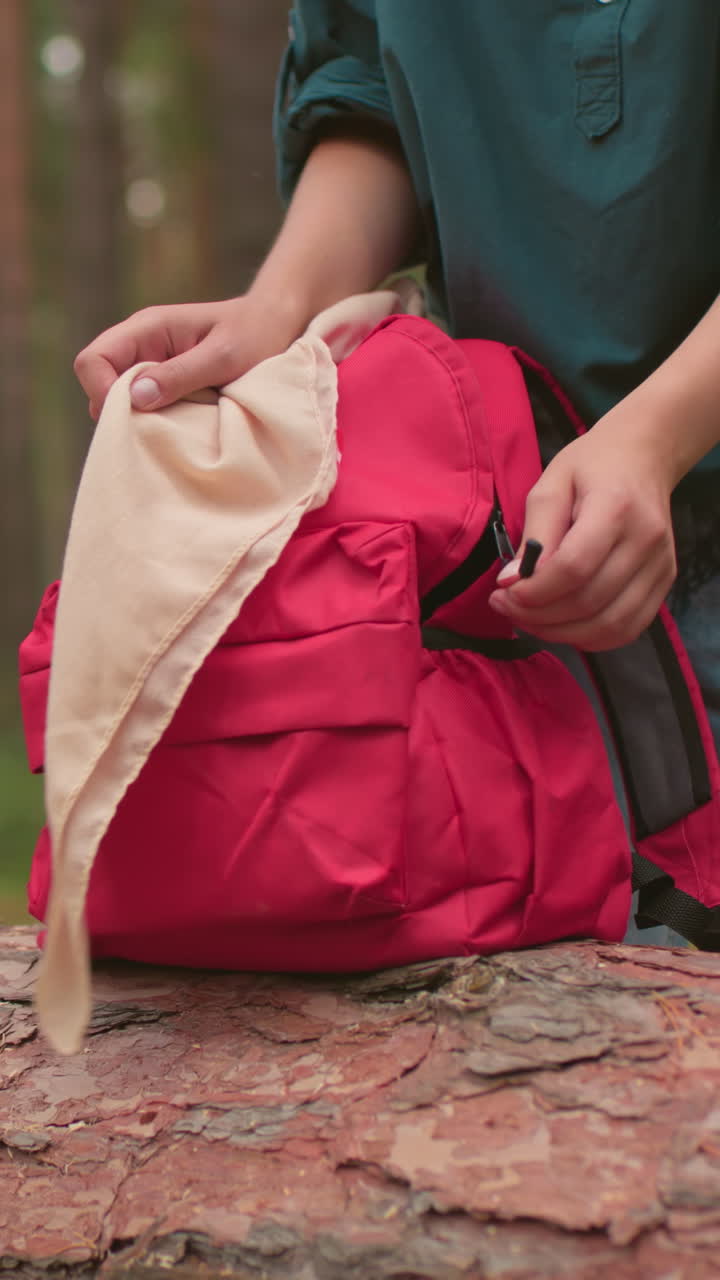 산책하는 사람들이 평온한 숲을 걸어다니며, 배을 들고, 하나는 초록색 셔츠를 입고 다른 하나는 회색 스웨터를 입고, 그들은 녹색 옷을 입은 여자가 빨간 가방을 열기 시작할 때 쓰러진 나무 근처에서 멈추고 있습니다.