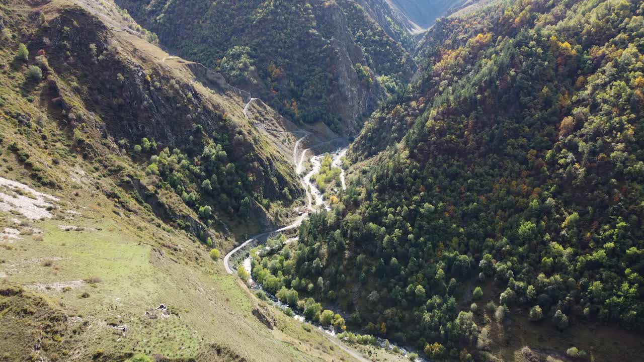 Drone aerial fly at a beautiful deep mountain valley with winding river and forested slopes in sunlight, Khevsureti, Mtskheta-Mtianeti, Georgia