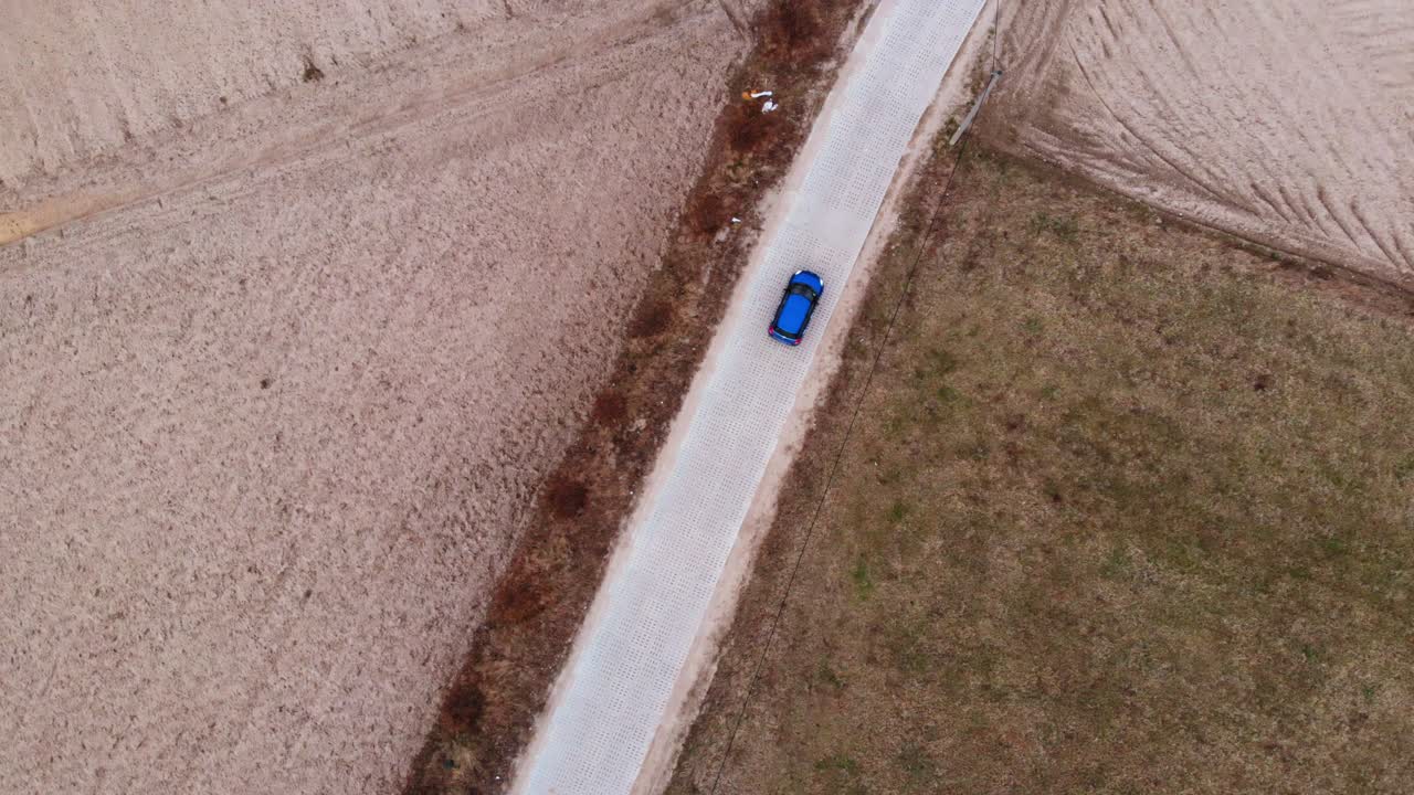 Un'auto blu percorre una strada deserta circondata da campi