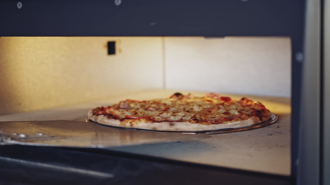 Pizza is getting ready in oven. Chef opening oven door and checking pizza readiness. Cook checks pizza for readiness using the pizza ring.