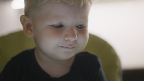 niño pequeño de ojos azules mira video en la pantalla del dispositivo brillante