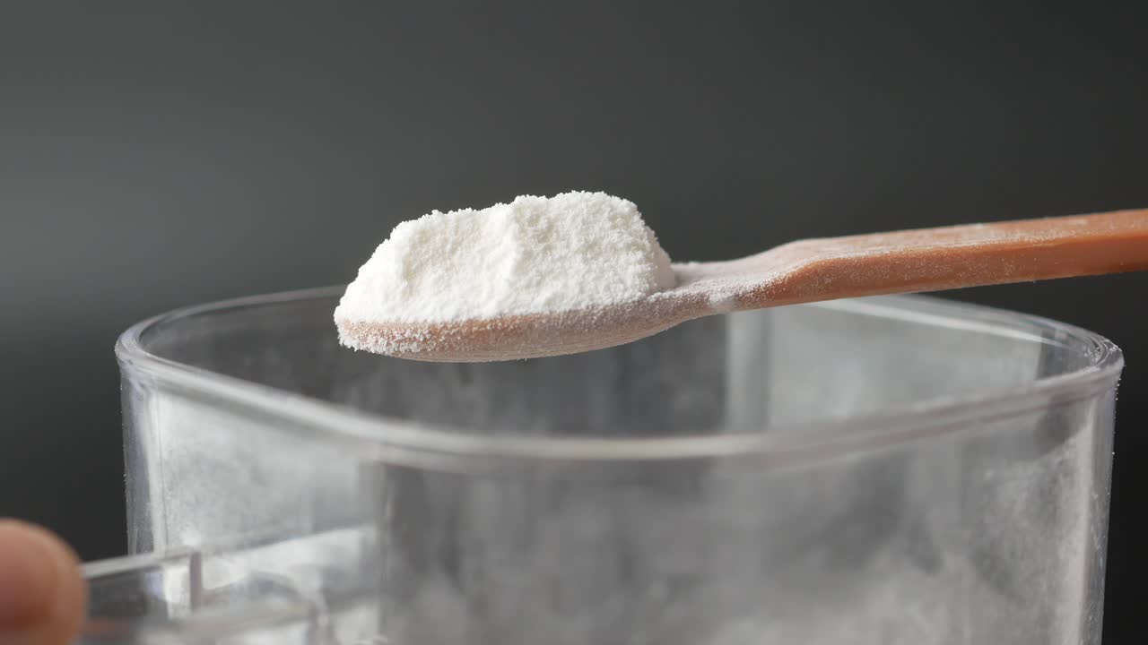 Close up of a wooden spoon scooping flour from a container