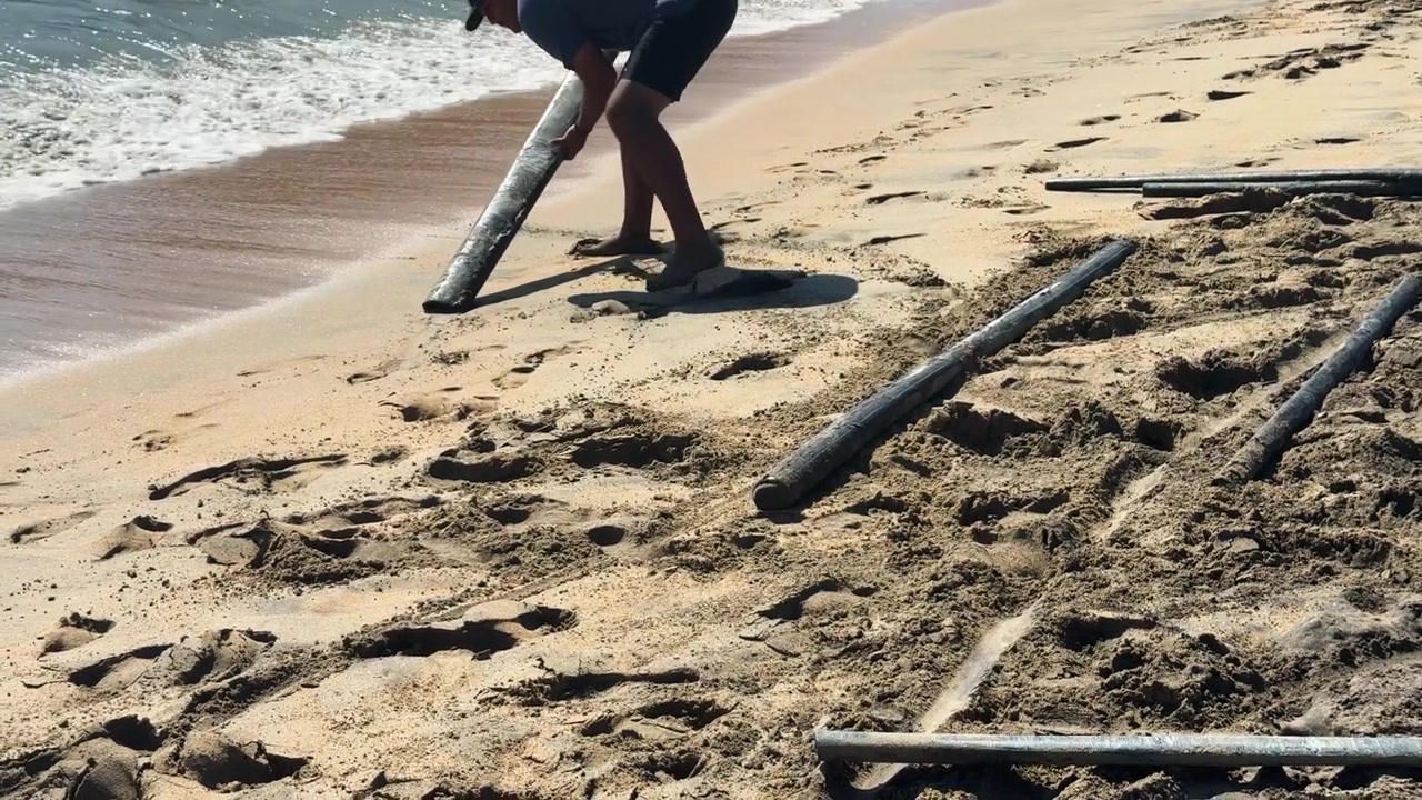 Un operaio posiziona tronchi di legno su una spiaggia sabbiosa vicino alle onde dell'oceano.
